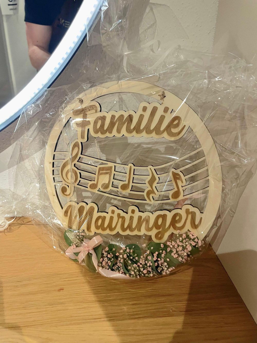 Holzloop mit dem Schriftzug „Familie Mairinger“, Notenlinien und Musiknoten, dekoriert mit Schleierkraut und Röschen