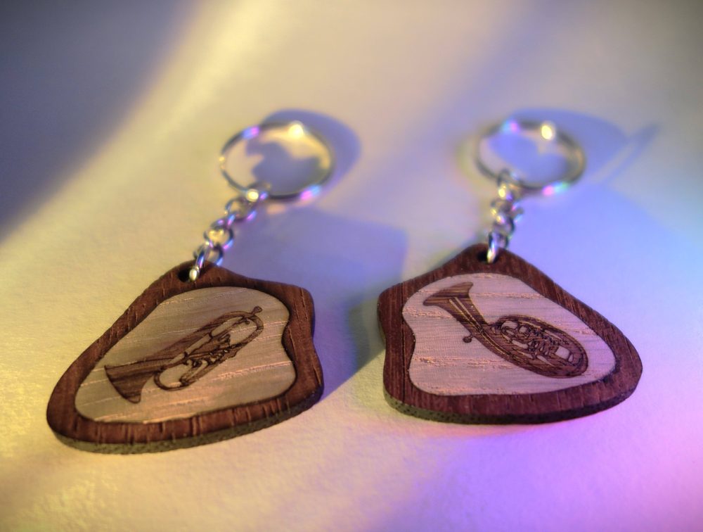 Zwei Schlüsselanhänger aus Holz mit dunklem Rand und gravierten Blechblasinstrumenten