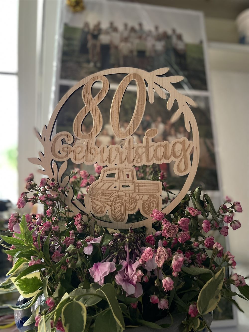 Personalisierter Tortenstecker aus hellem Holz mit der Gravur „80 Geburtstag“ und einem Fahrzeug-Motiv, in einem Strauß rosa Blumen